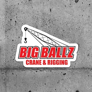 May include: White stickers with a red and black logo reading "BIG BALLZ" above "CRANE & RIGGING". The logo features a crane graphic. The stickers are on a grey concrete background.