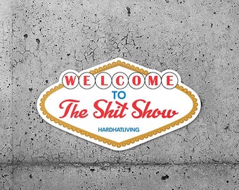 Puede incluir: Dos pegatinas blancas con un diseño rojo y azul. Las pegatinas tienen la forma del letrero de Las Vegas y dicen "Bienvenido al Show de la Mierda" con el texto "Hardhat Living" debajo.