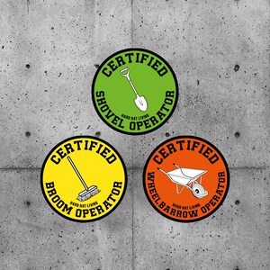 May include: Three round stickers with black borders and white text. Each sticker features a different tool: a shovel, a broom, and a wheelbarrow. The text on each sticker reads "Certified" and "Hard Hat Living" with the name of the tool in between.