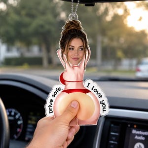 May include: A clear acrylic car air freshener ornament featuring a graphic illustration of a person in a red bikini with a photo-realistic face, accompanied by the printed text Drive safe. I Love you. hanging from a silver ball chain.