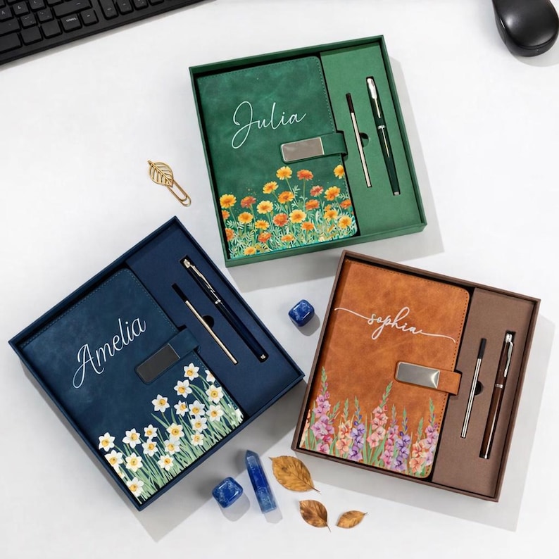 Puede incluir: Tres juegos de diario y bol&iacute;grafo personalizados en cajas de regalo. Los diarios son verdes, azules y marrones, cada uno con un dise&ntilde;o floral y un nombre. Cada juego incluye un bol&iacute;grafo a juego.