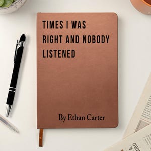 K&ouml;nnte beinhalten: Ein braunes Notizbuch mit dem Text "TIMES I WAS RIGHT AND NOBODY LISTENED" und "By Ethan Carter" in Schwarz gedruckt. Ein schwarzer Stift und ein silberner Stift befinden sich auf der linken Seite des Notizbuchs.