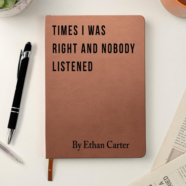 K&ouml;nnte beinhalten: Ein braunes Notizbuch mit dem Text "TIMES I WAS RIGHT AND NOBODY LISTENED" und "By Ethan Carter" in Schwarz gedruckt. Ein schwarzer Stift und ein silberner Stift befinden sich auf der linken Seite des Notizbuchs.