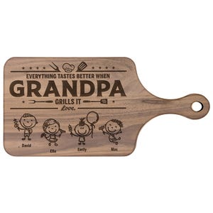 Może przedstawiać: Drewniana deska do krojenia z uchwytem, wygrawerowana słowami "Everything tastes better when Grandpa grills it." Poniżej tekstu znajdują się ilustracje postaci z patyk&oacute;w i imiona. Deska jest brązowa.
