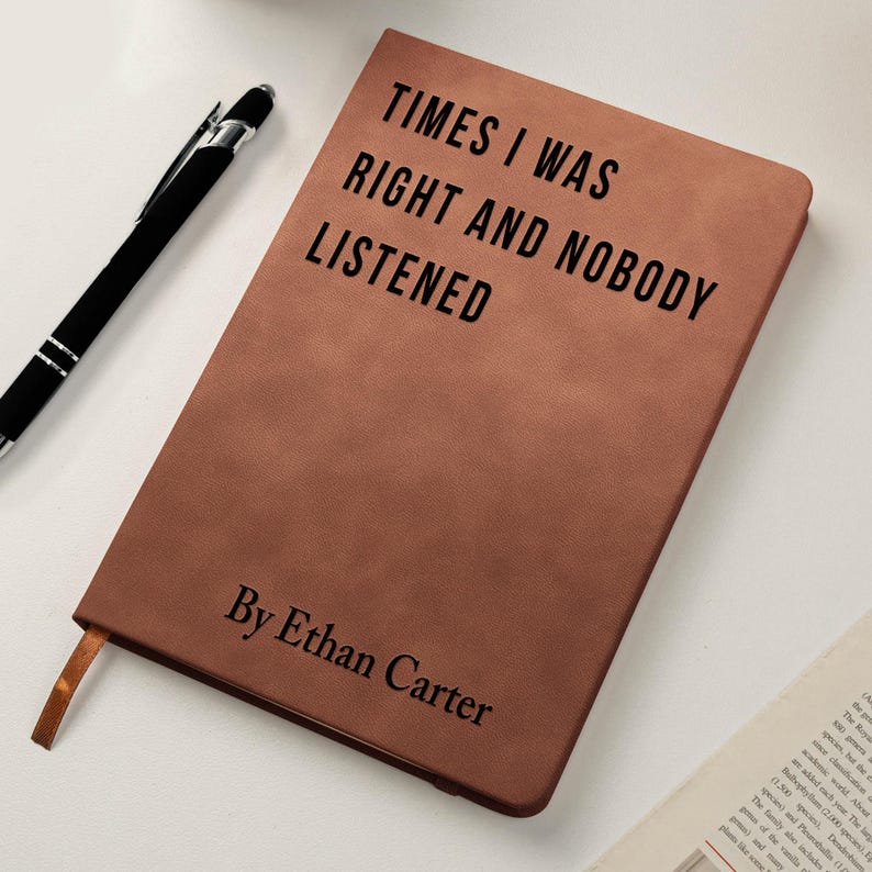 K&ouml;nnte beinhalten: Ein braunes Lederjournal mit dem Text "TIMES I WAS RIGHT AND NOBODY LISTENED" und "By Ethan Carter" in Schwarz gedruckt. Ein schwarzer Stift liegt neben dem Journal, was auf ein Schreibthema hindeutet.