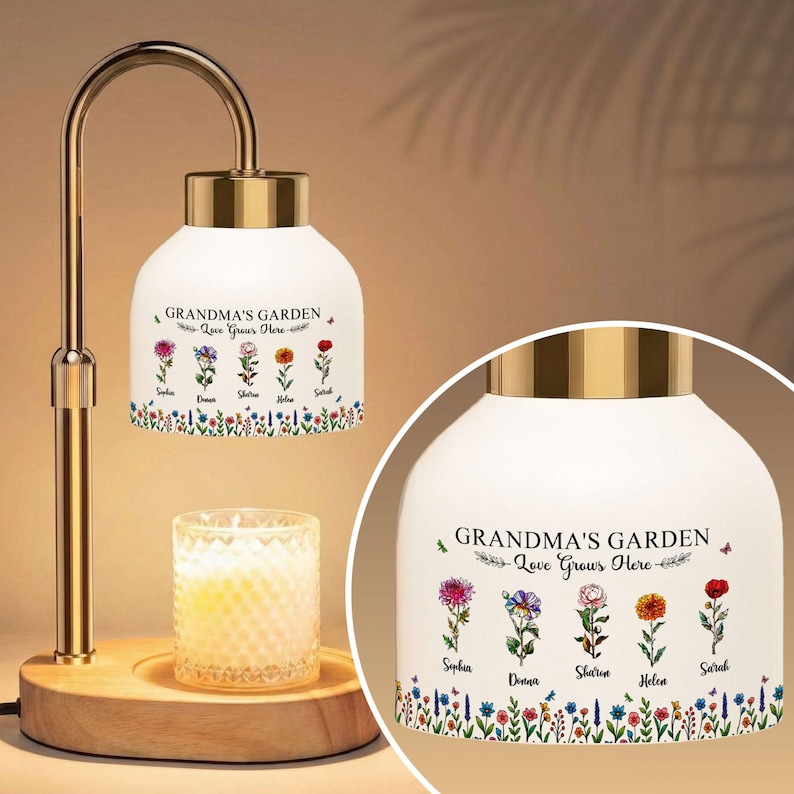 May include: A decorative lamp with a white shade featuring the text "GRANDMA'S GARDEN Love Grows Here" and floral illustrations. The lamp has a gold-colored metal frame and a wooden base. A lit candle sits below the shade.