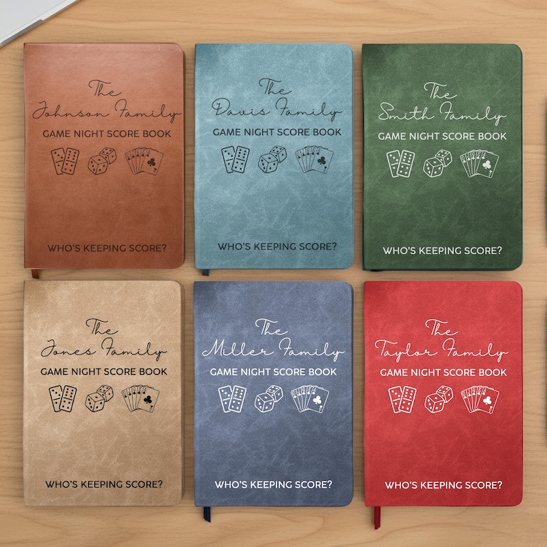 May include: Six rectangular game night score books in brown, light blue, green, tan, dark blue, and red. Each cover features a family name, the text GAME NIGHT SCORE BOOK, illustrations of dominoes, dice, and playing cards, and WHO'S KEEPING SCORE?