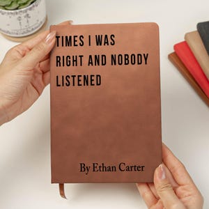 K&ouml;nnte beinhalten: Ein braunes Lederjournal, das von H&auml;nden gehalten wird, mit dem Text "TIMES I WAS RIGHT AND NOBODY LISTENED" und "By Ethan Carter" in Schwarz gedruckt. Ein Lesezeichen aus Band ist sichtbar. Weitere Journale in verschiedenen Farben sind im Hintergrund.