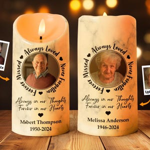Peut inclure: Deux bougies commémoratives blanches avec un effet marbré. Chaque bougie comporte un cadre photo avec une bordure noire et le texte "Always Loved, Forever Missed, Never Forgotten" en cercle autour de la photo. Le texte "Always in our Thoughts, Forever in our Hearts" est sous le cadre photo. Le nom et les dates du défunt sont sous le texte. Les bougies sont sur une surface en bois.