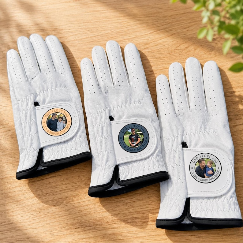 K&ouml;nnte beinhalten: Drei wei&szlig;e Golfhandschuhe mit schwarzem Besatz und perforierten Fingern. Jeder Handschuh hat einen runden Aufn&auml;her am Handgelenkriemen, der ein Foto einer Person mit einem Kind und den Text DAD I LOVE YOU TO THE ROUGH AND BACK zeigt.