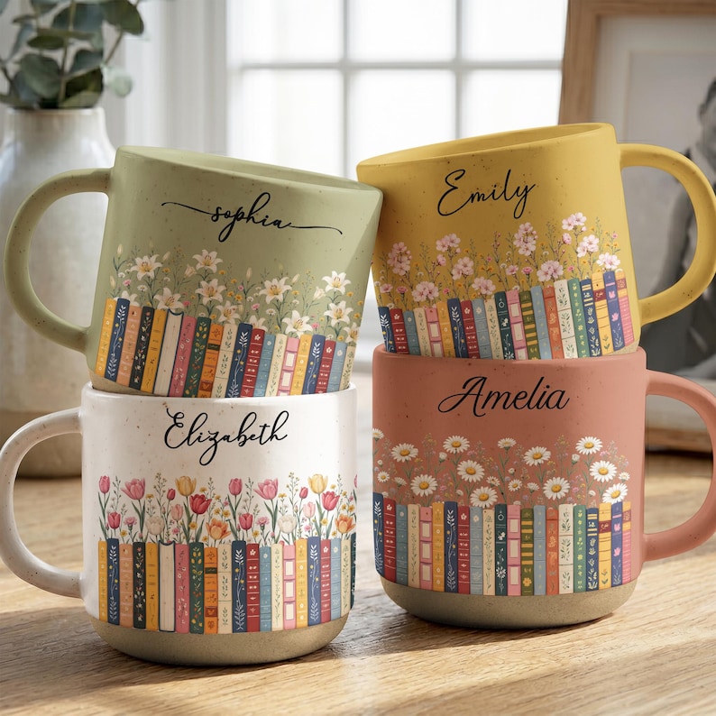 May include: Four ceramic mugs with speckled finishes, each featuring a unique color, a row of colorful book spines, floral illustrations, and a personalized name in black script: Sophia on sage green, Emily on yellow, Elizabeth on white, and Amelia on terracotta.