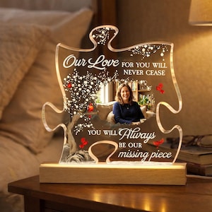 May include: A clear acrylic puzzle piece-shaped night light with a photo of a woman. The light has the words "Our Love" and "Always be our missing piece" etched on it. The light sits on a wooden base.