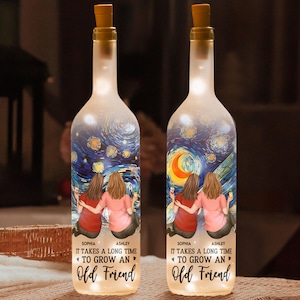 May include: Two illuminated wine bottles with cork stoppers. Each bottle features a painting of two friends and a starry night sky. The text reads "IT TAKES A LONG TIME TO GROW AN Old Friend".