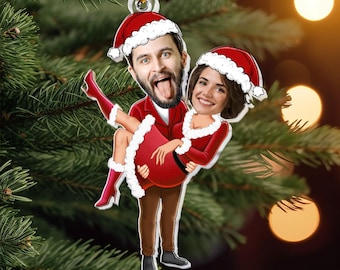 May include: A Christmas ornament featuring a cartoon couple dressed in Santa suits. The man is holding the woman in his arms.