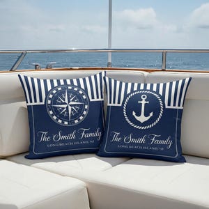 May include: Two navy blue nautical cushions with white striped borders. One cushion features a compass rose design, the other an anchor within a rope circle. Both cushions display "The Smith Family" and "Long Beach Island, NJ" in white text.