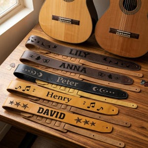 May include: Five leather guitar straps in varying shades of brown and black, each personalized with a name: LILY, ANNA, Peter, Henry, and DAVID. The straps feature engraved designs including birds, butterflies, moon phases, musical notes, and stars.