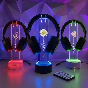 May include: Three clear acrylic headphone stands with LED bases in red, blue, and green. Each stand features a unique floral graphic and a name: Diana, Chloe, or Sophia. The stands hold black over-ear headphones, and a small remote control is included.