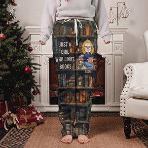 May include: Cozy pajama pants featuring a bookshelf design with the text "JUST A GIRL WHO LOVES BOOKS" and a cartoon illustration of a girl reading. The pants are dark with a drawstring waist.