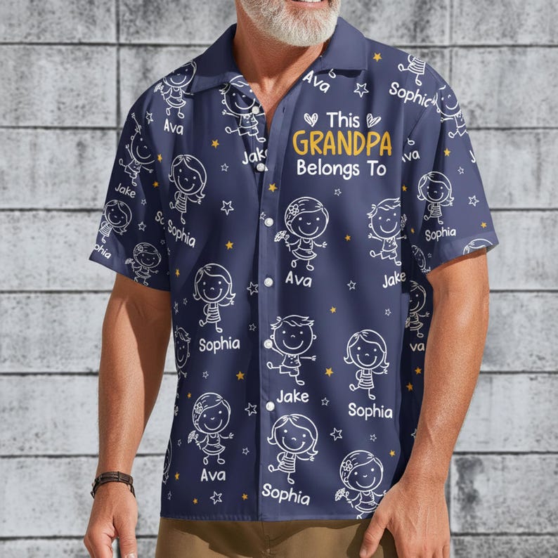 Peut inclure: Chemise bleu marine &agrave; manches courtes orn&eacute;e d'un motif r&eacute;p&eacute;t&eacute; de dessins d'enfants et d'&eacute;toiles. Le texte "This Grandpa Belongs To" est en or, avec des noms comme Ava, Jake et Sophia. Chemise boutonn&eacute;e.