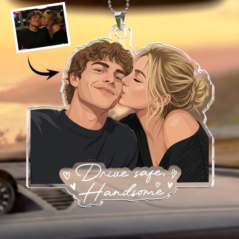 Puede incluir: Un adorno de coche de acr&iacute;lico transparente con una ilustraci&oacute;n personalizada de una pareja, donde una persona besa a la otra en la mejilla. El texto "Drive safe, Handsome" est&aacute; impreso en la parte inferior con corazones. Incluye una foto.