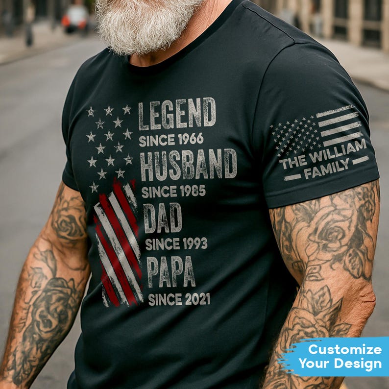 May include: Black t-shirt with a distressed American flag design and text. The text includes "LEGEND SINCE 1966", "HUSBAND SINCE 1985", "DAD SINCE 1993", and "PAPA SINCE 2021". The sleeve features an American flag and "THE WILLIAM FAMILY".