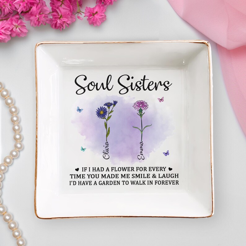 May include: A white ceramic trinket tray with a gold rim features a watercolor design of two flowers with the text "Soul Sisters" and the names "Olivia" and "Emma". The text below the flowers reads "If I had a flower for every time you made me smile & laugh I'd have a garden to walk in forever."
