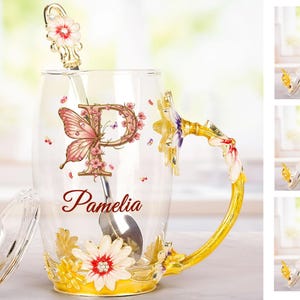 May include: A glass mug with a gold handle and floral accents. The mug has a butterfly and the letter "P" on it. The mug also has the name "Pamela" written on it. The mug comes with a lid and a spoon.