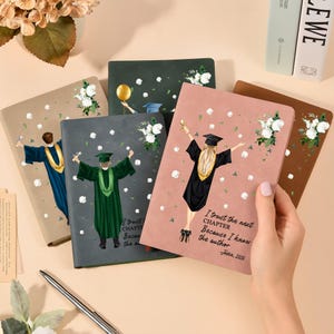 May include: A collection of graduation-themed notebooks. Each notebook features a different color and illustration of a graduate in a cap and gown. One notebook has the text "I trust the next chapter because I know the author".