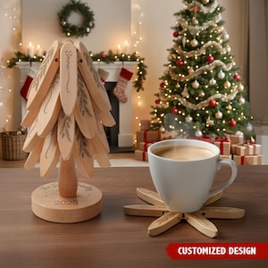 May include: A wooden Christmas tree with personalized name tags and a base that reads "The S Family 2025". A white mug of coffee sits on a wooden coaster. A decorated Christmas tree and fireplace are in the background.