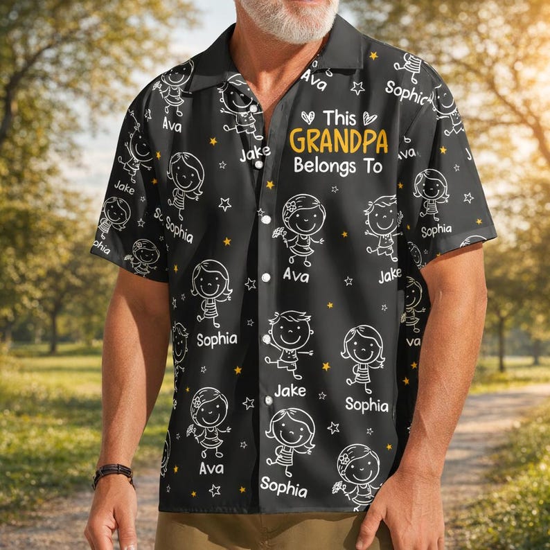 Peut inclure: Chemise noire &agrave; boutons avec un motif r&eacute;p&eacute;t&eacute; de dessins d'enfants et d'&eacute;toiles. La chemise porte l'inscription "This GRANDPA Belongs To" en jaune, avec des noms comme Ava, Jake et Sophia.