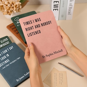 K&ouml;nnte beinhalten: Eine Person h&auml;lt ein rosa Notizbuch mit dem Text "TIMES I WAS RIGHT AND NOBODY LISTENED" und "By Sophia Mitchell". Weitere Notizb&uuml;cher in Gr&uuml;n, Braun und Blau sind sichtbar, mit Texten wie "CLEVER COMEBACKS" und "...And Other Workplace Tales".