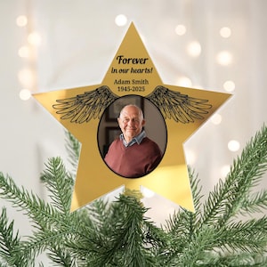 Peut inclure: Ornement commémoratif en forme d'étoile dorée avec une photo d'un homme en pull marron. L'ornement porte l'inscription "Forever in our hearts!" et "Adam Smith 1945-2025" avec des ailes. L'ornement est sur un sapin de Noël.
