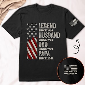 May include: Black t-shirt featuring an American flag design with text: "LEGEND SINCE 1966, HUSBAND SINCE 1985, DAD SINCE 1993, PAPA SINCE 2021." The sleeve has the text "THE WILLIAM FAMILY." A circular inset shows the same design.