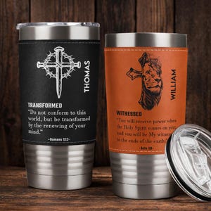 May include: Two stainless steel insulated tumblers with black and orange leather wraps. One features a cross and the word "TRANSFORMED" with a Bible verse. The other has a lion and cross with the word "WITNESSED" and a Bible verse.