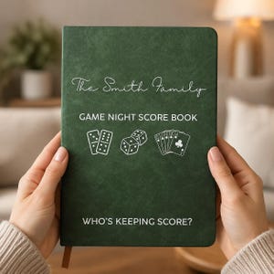 May include: A dark green rectangular score book with white text that reads The Smith Family, GAME NIGHT SCORE BOOK, and WHO'S KEEPING SCORE? The cover features white line art illustrations of two dominoes, two dice, and a hand of playing cards.