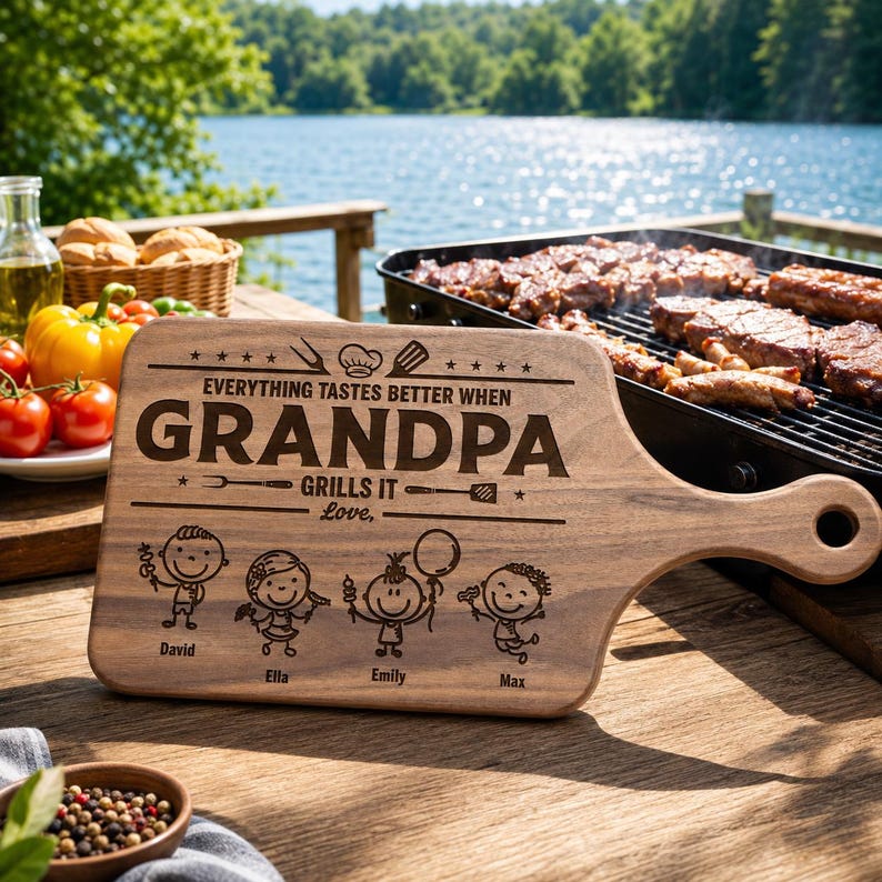 Może przedstawiać: Drewniana deska do krojenia z uchwytem, ​​z wygrawerowanymi słowami "EVERYTHING TASTES BETTER WHEN GRANDPA GRILLS IT Love" oraz imionami David, Ella, Emily i Max. Deska jest brązowa i ma naturalne usłojenie drewna.