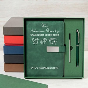 May include: A green game night score book with a silver metal clasp, featuring the text The Johnson Family GAME NIGHT SCORE BOOK and WHO'S KEEPING SCORE? along with icons of dice and playing cards, presented in a box with a matching green pen.