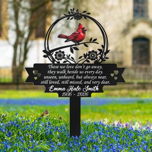 May include: A black metal memorial stake with a red cardinal perched on a branch within a floral frame. The stake features a banner with a heartfelt message and the name "Emma Hale Smith" with the years 1936-2026.