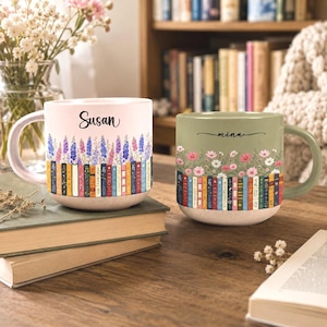 May include: Two ceramic mugs featuring a row of colorful book spines at the base topped with floral illustrations. The left mug is light pink with the name Susan, while the right mug is sage green with the name mina printed in black script.
