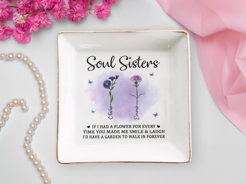 May include: White ceramic trinket tray with gold trim featuring a watercolor design of two flowers with the text "Soul Sisters" and the names "Olivia" and "Emma" below the flowers. The text below the flowers reads "If I had a flower for every time you made me smile & laugh I'd have a garden to walk in forever."
