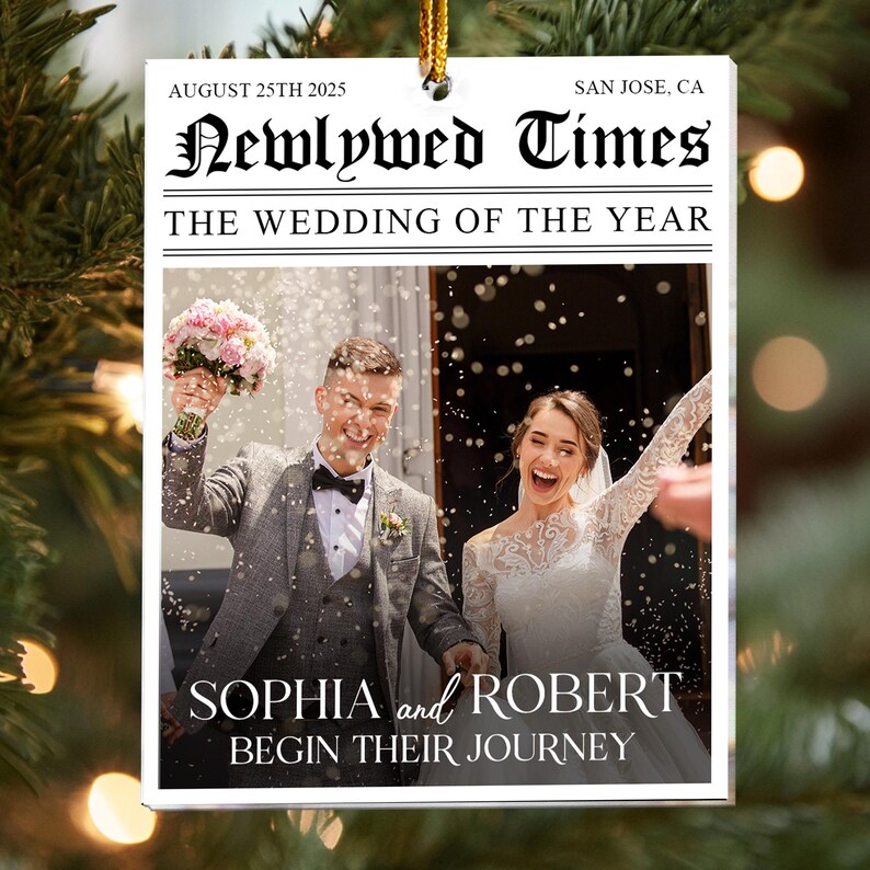 May include: A rectangular white ornament featuring a newspaper-style design titled Newlywed Times. It includes the text August 25th 2025, San Jose, CA, The Wedding of the Year, and Sophia and Robert Begin Their Journey, with a photo of a couple.