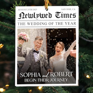 May include: A rectangular white ornament featuring a newspaper-style design titled Newlywed Times. It displays the text August 25th 2025, San Jose, CA, and The Wedding of the Year. A photo shows a couple with a bouquet and confetti, labeled Sophia and Robert Begin Their Journey.