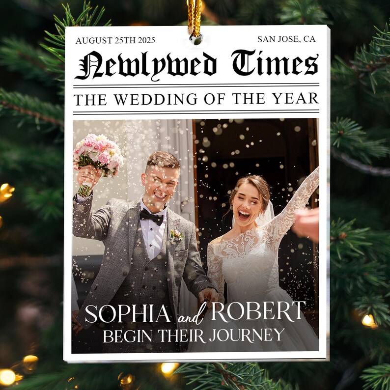 May include: A rectangular white ornament featuring a newspaper-style design titled Newlywed Times. It displays the text August 25th 2025, San Jose, CA, and The Wedding of the Year. A photo shows a couple with a bouquet and confetti, labeled Sophia and Robert Begin Their Journey.