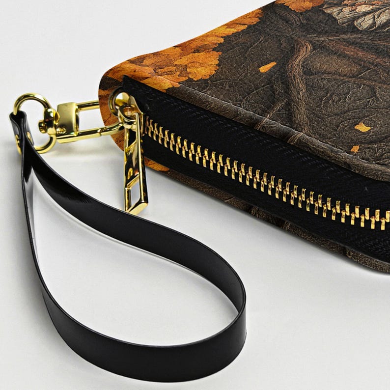 May include: A close-up of a wallet with a black zipper and a gold-colored zipper pull. The wallet has a black wrist strap and a brown and yellow patterned design.