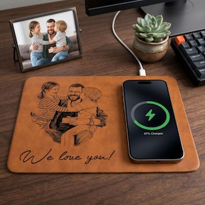 May include: A brown leather desk mat with a family portrait and the text "We love you!". A smartphone charging on the mat displays a charging symbol and 67% charged. A framed photo and a succulent plant are also on the desk.
