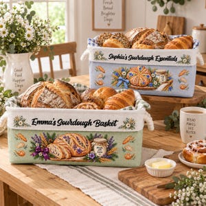 May include: Two rectangular fabric storage baskets filled with assorted breads. The front basket is sage green with the text Emma's Sourdough Basket, while the back basket is light blue with the text Sophia's Sourdough Essentials, both featuring floral and bread illustrations.