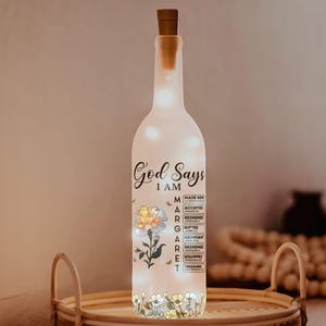 May include: A decorative light-up bottle with a cork stopper. The bottle is illuminated with small lights and features the text "God Says I AM" along with floral and bee designs. The bottle also lists positive affirmations.