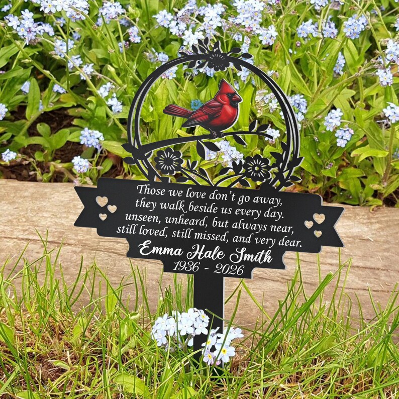 May include: A black metal memorial garden stake featuring a red cardinal perched on a branch within a circular frame. The stake includes a banner with the text "Those we love don't go away..." and the name "Emma Hale Smith 1936-2026."