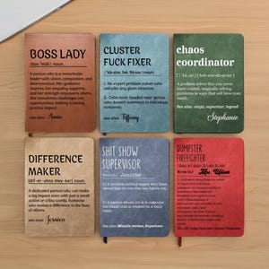 May include: Six notebooks with humorous definitions, such as "BOSS LADY" and "DUMPSTER FIREFIGHTER." Each notebook is a different colour and features a definition. The notebooks are displayed on a light-coloured surface.