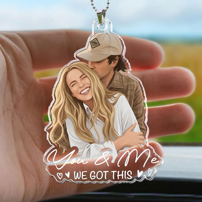 Puede incluir: Un adorno colgante de acr&iacute;lico transparente con una ilustraci&oacute;n de dibujos animados de una persona rubia sonriente abrazando a otra con gorra de b&eacute;isbol beige y camisa a cuadros. El texto "You & Me WE GOT THIS" est&aacute; impreso en letras blancas.